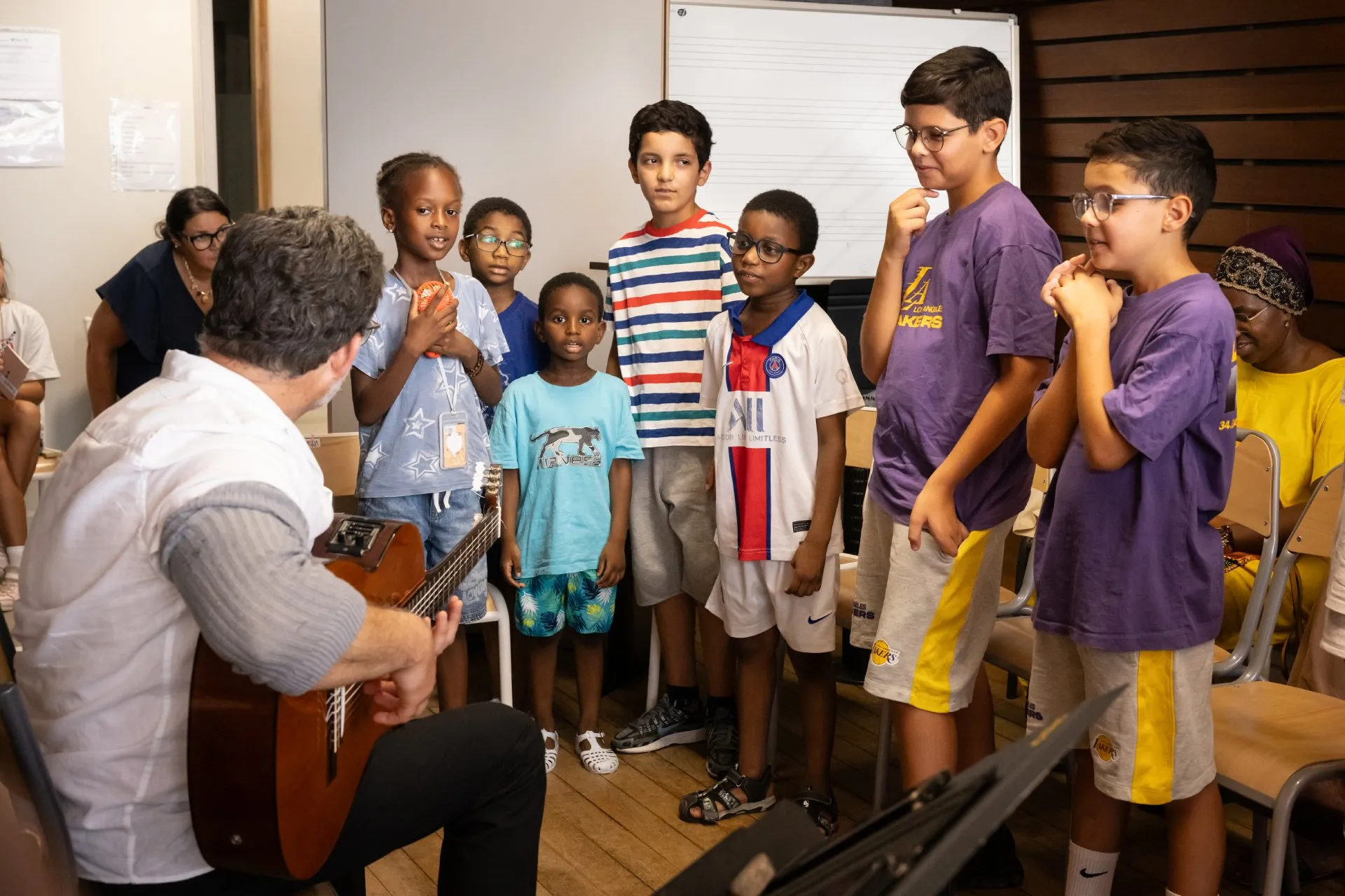Un homme assis en train de jouer de la guitare avec un groupe d'enfants autour de lui